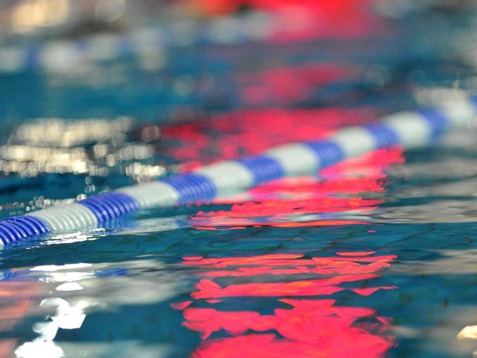 Reflektion einer blauen und weißen Schwimmbahn in klarem Wasser mit unscharfen Lichtern im Hintergrund.
