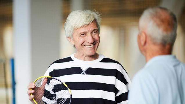 Zwei ältere Männer unterhalten sich im Badminton-Sportzentrum, einer hält einen Badmintonschläger in der Hand.