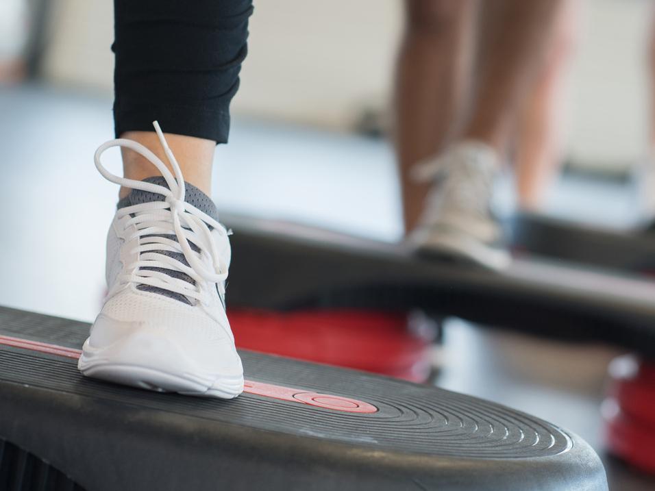 Nahaufnahme eines Fußs mit einem weißen Sport-Schuh auf einer Fitness-Stepp-Platte während eines Workout.
