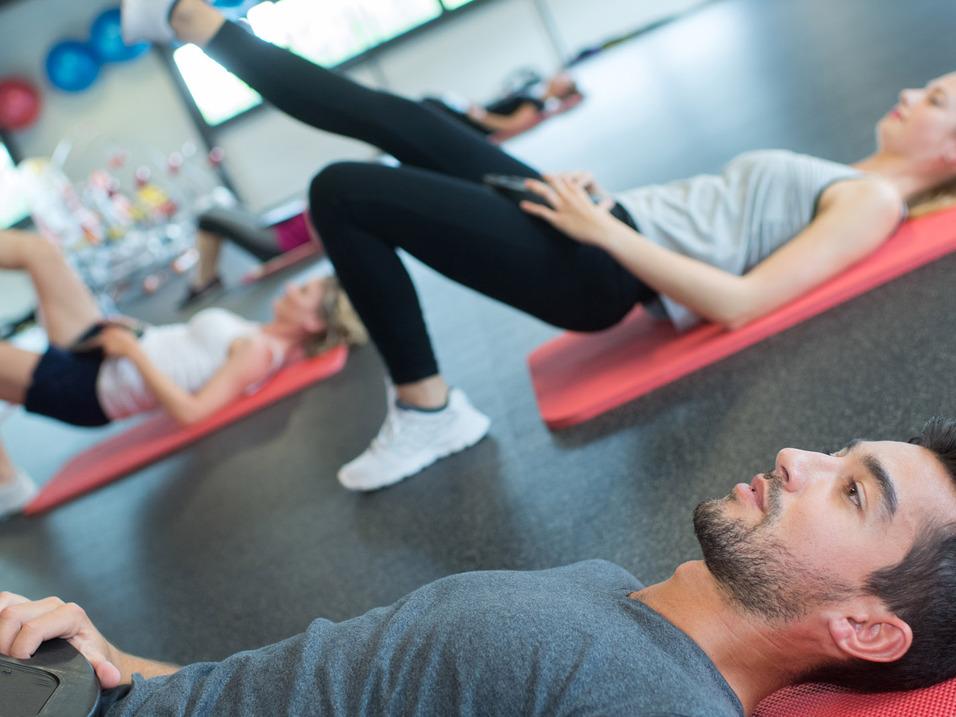 Gruppe von Menschen bei einem Workout, einige auf Fitnessmatten mit Gewichten, andere in Bauchlage.
