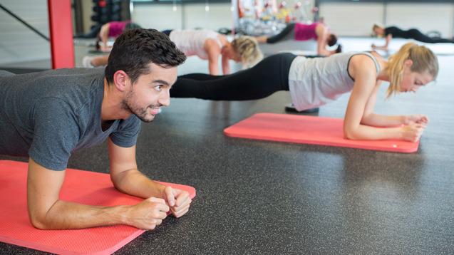 Mann und Frauen machen Plank-Übungen auf Yogamatten in einem Fitnessstudio. Helle, sportliche Atmosphäre.