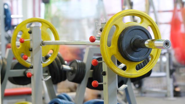 Nahaufnahme einer Langhantel mit gelben und schwarzen Gewichten in einem Fitnessstudio.