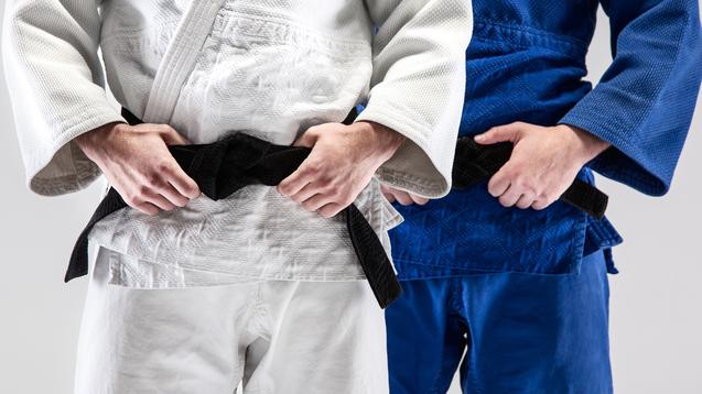 Zwei Judokas im weißen und blauen Gi halten einen schwarzen Gürtel vor ihrem Bauch.