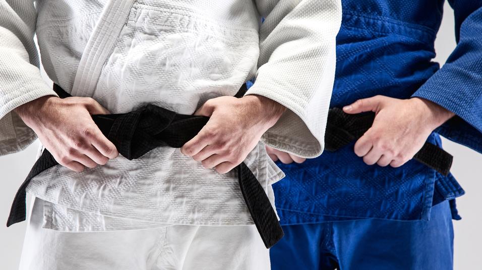 Zwei Judokas im weißen und blauen Gi halten einen schwarzen Gürtel vor ihrem Bauch.