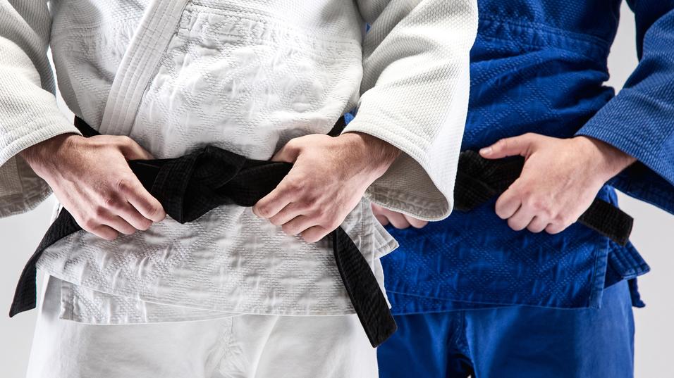 Zwei Judokas im weißen und blauen Gi halten einen schwarzen Gürtel vor ihrem Bauch.