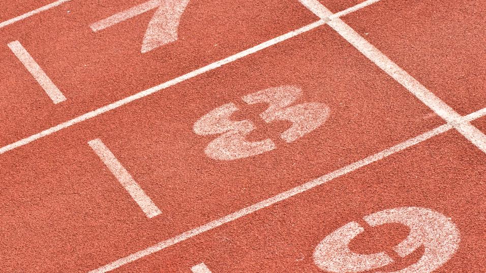 Nahaufnahme von Laufbahnmarkierungen mit den Nummern 7, 8 und 9 auf einem roten Sportplatz.