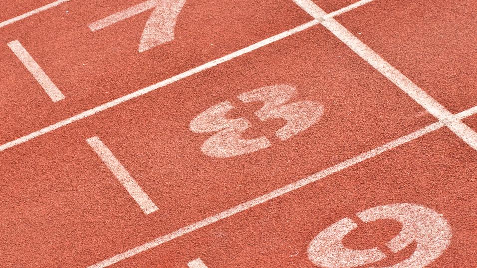 Nahaufnahme von Laufbahnmarkierungen mit den Nummern 7, 8 und 9 auf einem roten Sportplatz.