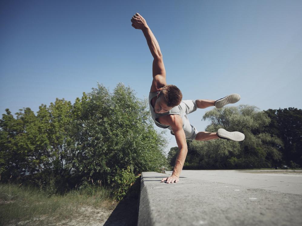 Ein junger Mann balanciert auf einer Mauer und streckt einen Arm in die Luft, um sein Gleichgewicht zu halten.