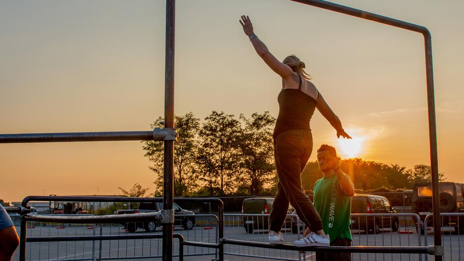 Zwei Personen üben auf einem Stangen-Gerüst bei Sonnenuntergang, während eine Person zuschaut.