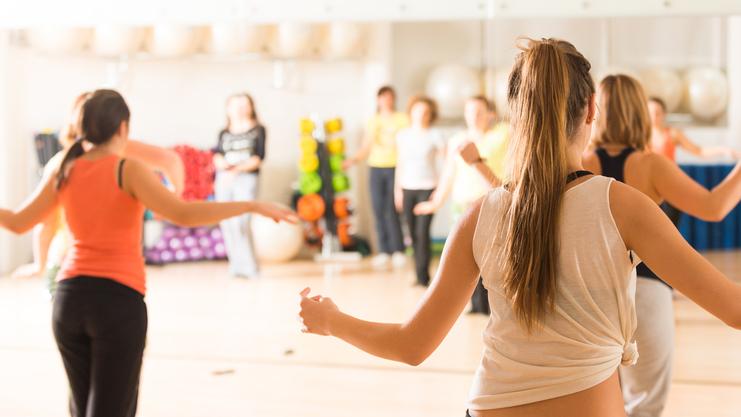 Gruppe von Frauen in Sportkleidung beim Tanztraining in einem gut beleuchteten Fitnessraum mit Spiegeln.
