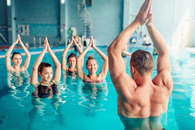 Acht Personen, die im Wasser stehen, führen gemeinsam eine Übung mit erhobenen Händen durch.