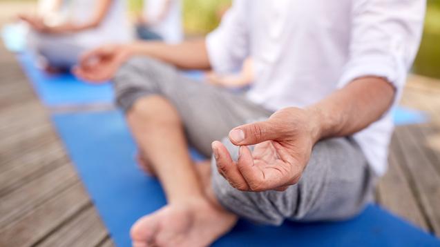 Nahaufnahme einer Hand, die im Meditationszustand auf einer blauen Yogamatte liegt, mit Fuß im Vordergrund.